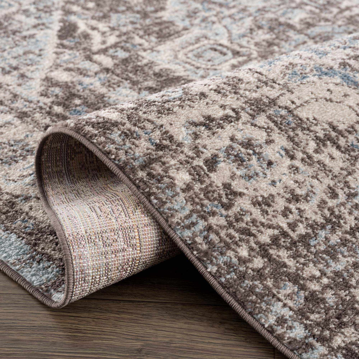 Dark brown medallion area rug by Hauteloom, folded to show intricate pattern and plush texture in a studio setting.